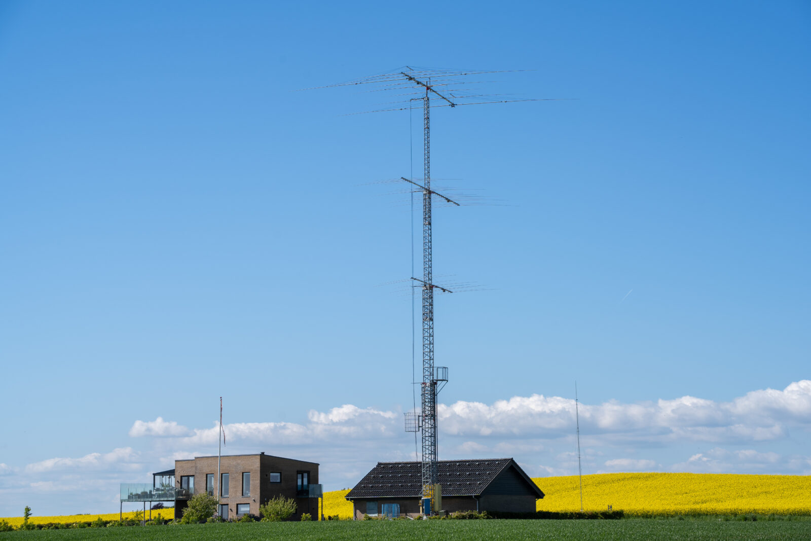 Grunden er købt, og huset placeret, så det står højt og frit – den ideelle placering for masten. Parcellen blev udstykket som en bid af en landmands mark, så der var ingen omkringboende, der skulle spørges om lov. Derfor var det ret nemt at få byggetilladelse. Det var næppe gået, hvis Anders havde forsøgt at rejse masten på Grenåvej. Den lille mast til højre, der ”kun” er på højde med flagstangen, er til forsøg ved lav frekvens under 3 MHz.